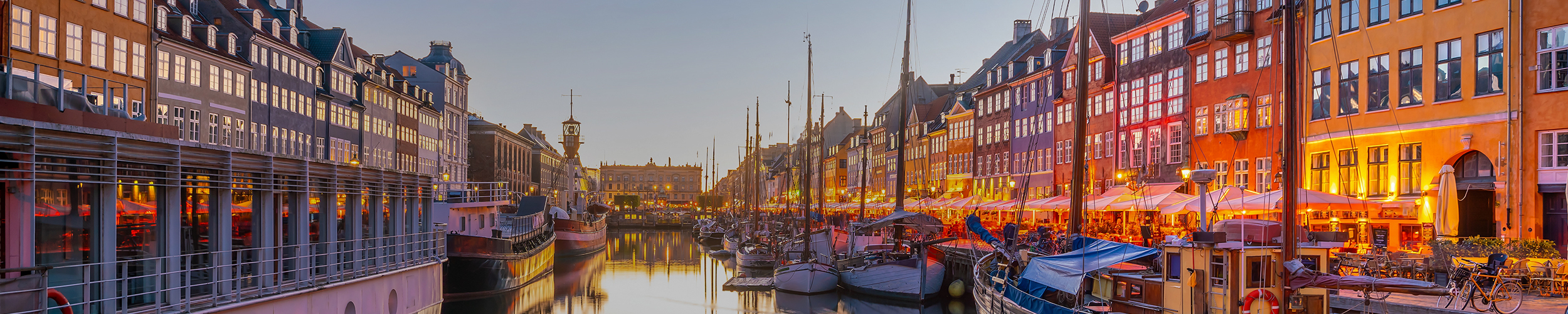 Panoramic view of Copenhagen waterfront with historic buildings, including the dome of Frederik's Church, and boats on the water under a partly cloudy sky. SPIE Astronomical Telescopes + Instrumentation will be hosted in Copenhagen.