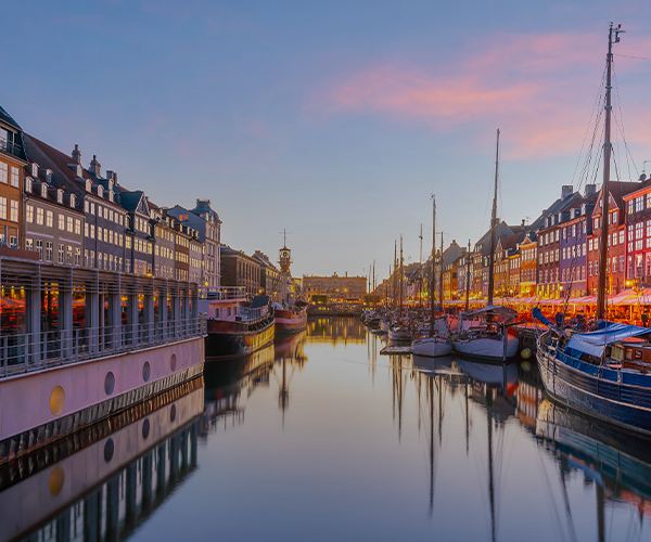 Panoramic view of Copenhagen waterfront with historic buildings, including the dome of Frederik's Church, and boats on the water under a partly cloudy sky. SPIE Astronomical Telescopes + Instrumentation will be hosted in Copenhagen.