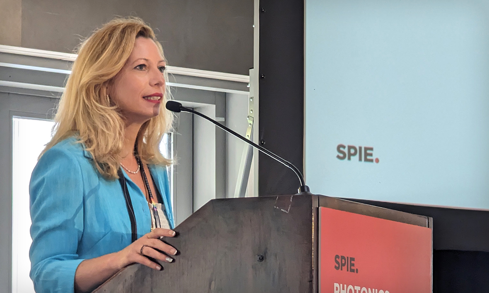 A woman in a blue blazer presents behind a podium at SPIE Photonics Industry Summit