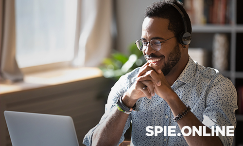 Person wearing headphones and a patterned shirt sitting at a desk with a laptop, with SPIE Online text in the corner.