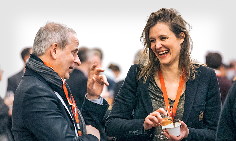 Two conference attendees wearing event lanyards talk and laugh together during a member networking reception.