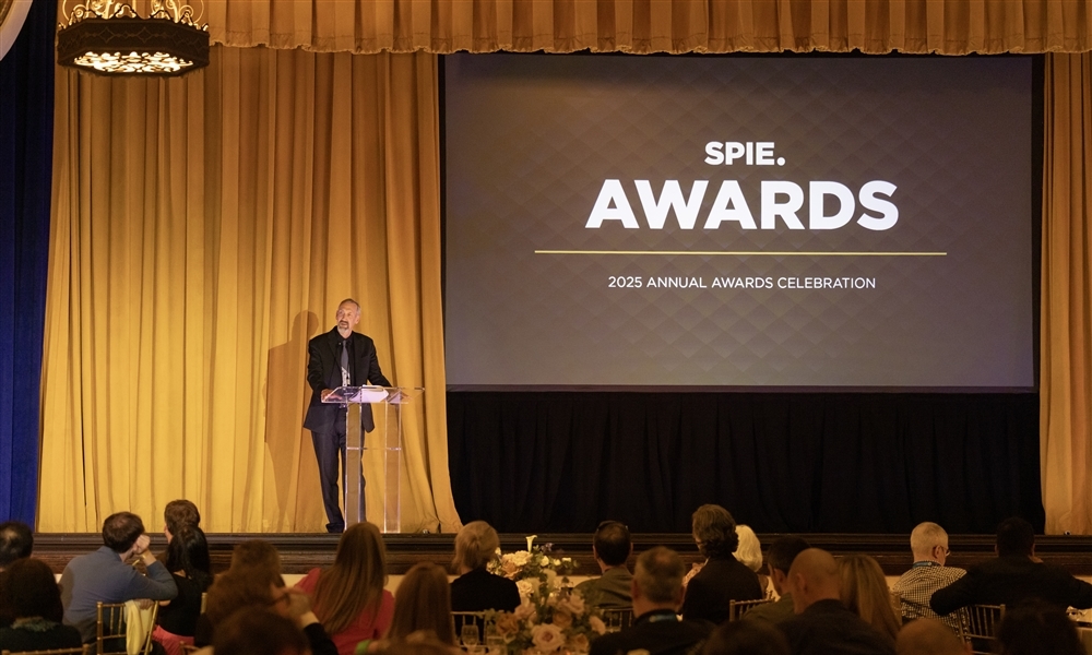 Speaker standing at a podium on stage during the SPIE Awards 2025 Annual Awards Celebration, with guests seated at tables and a large screen displaying the event title.