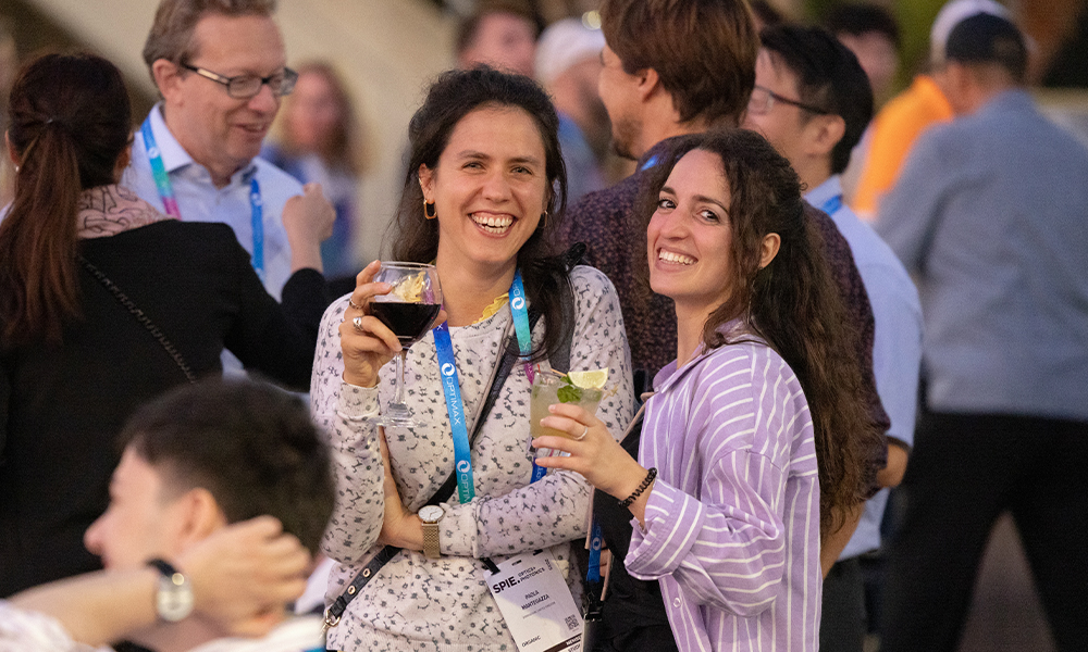 A large outdoor group, with two people smiling and holding drinks, looking at the camera. 