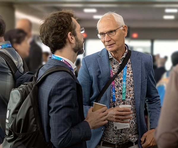 People networking in a bright conference hallway, wearing name badges and talking in small groups during SPIE Optics + Photonics,