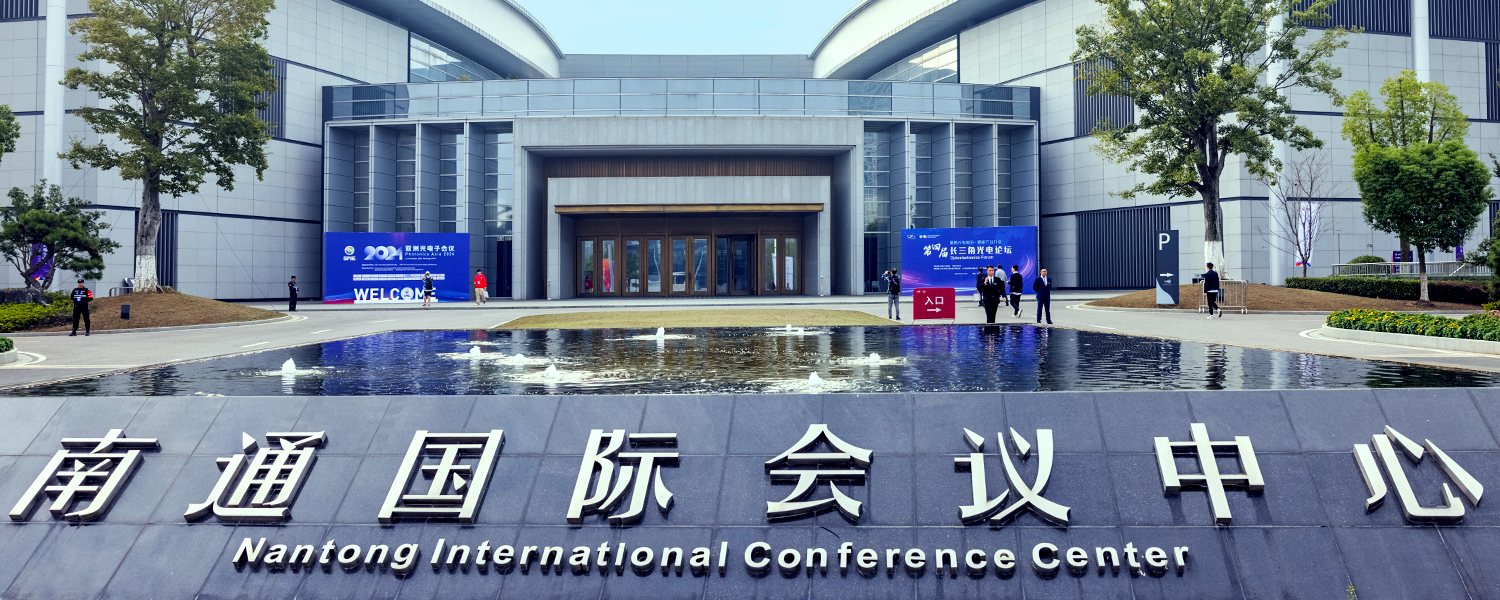 Exterior of the Nantong International Conference Center, showing a modern glass-and-stone building with a wide entrance, a reflecting pool in the foreground, and signage in Chinese and English reading ‘Nantong International Conference Center.