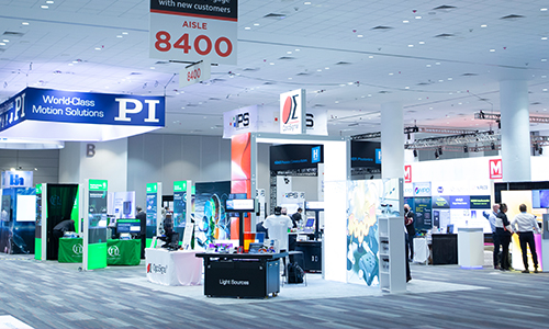 Wide view of a trade show floor with exhibitor booths, signage, and an overhead aisle 8400 marker.