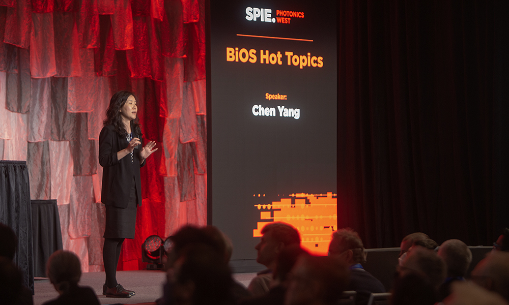 Speaker presenting at SPIE Photonics West conference on the topic of 'BiOS Hot Topics', with the speaker's name, Chen Yang, displayed on a screen behind them.