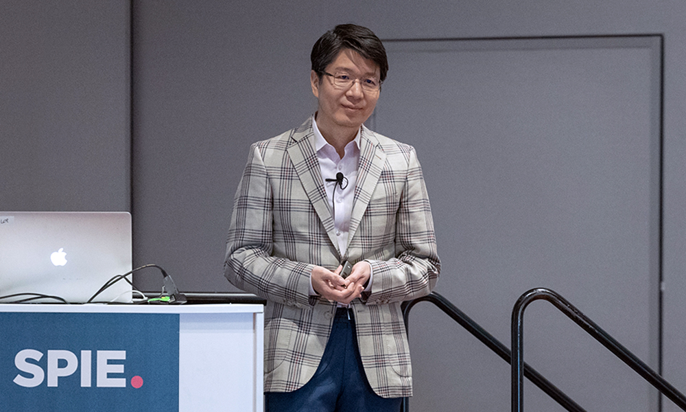 SPIE Photonics West author presents their research beside a podium with a sign that says SPIE.
