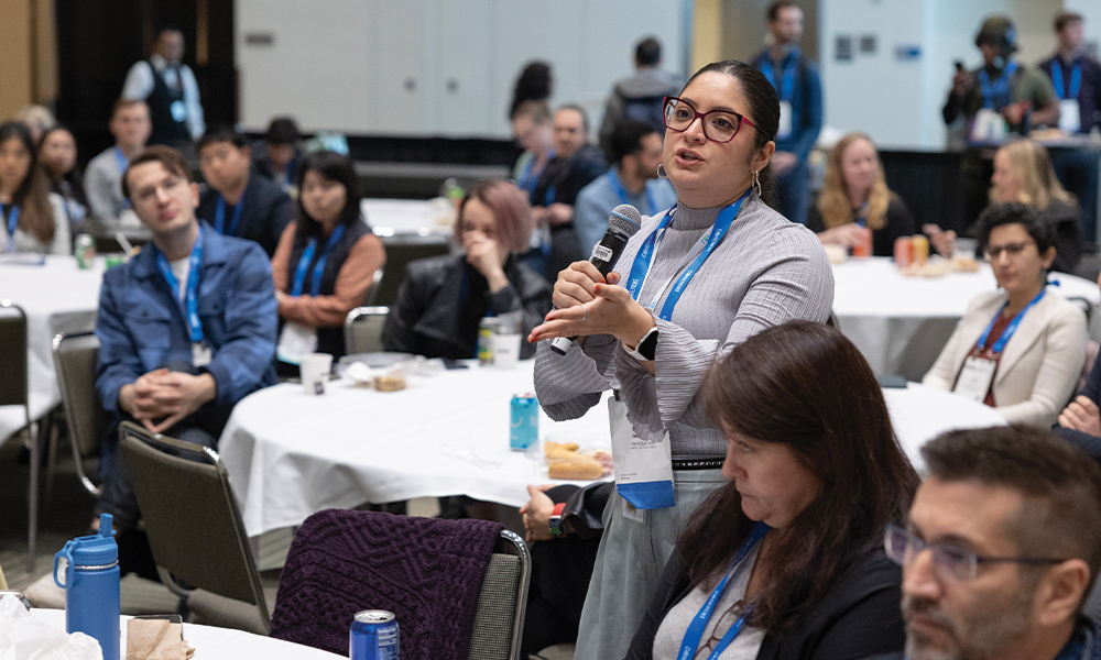 wo attendees walk and talk at SPIE Photonics West 2023, wearing conference badges and lanyards, with booths and other participants visible in the background.