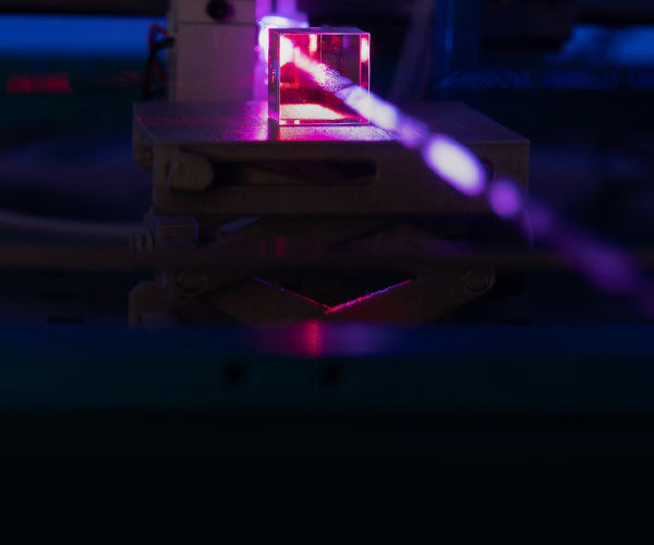A purple laser shoots towards the viewer through a square glass lens