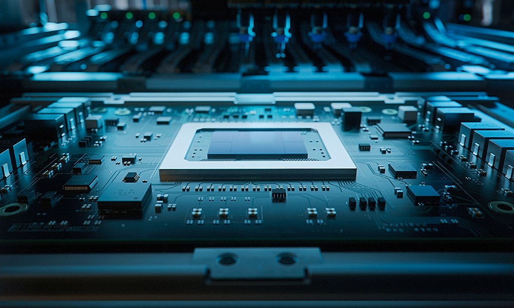 Close-up view of an electronic circuit board inside a computing system, featuring a rectangular central processor or chip socket mounted on a dark teal motherboard. Surrounding the chip are fine traces, capacitors, and integrated components arranged in precise rows.