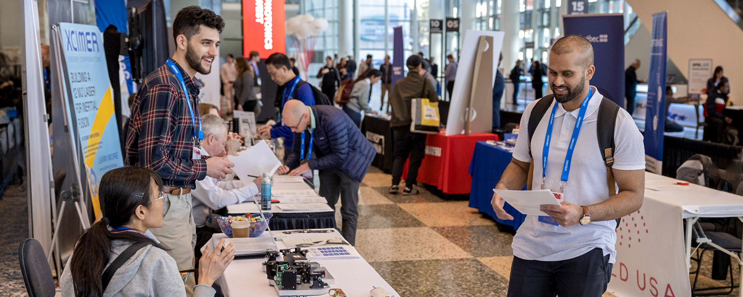 Three students at a conference are talking and smiling around an event table. They are wearing name tags.