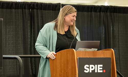 A woman presents a professional development course from a podium with the SPIE logo during an indoor conference session.