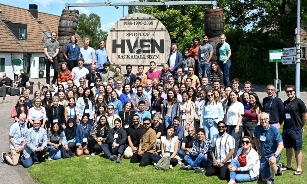 Large group of SPIE Biophotonics Summer School participants gathered outdoors for a group photo in front of a “Spirit of Hven” sign.