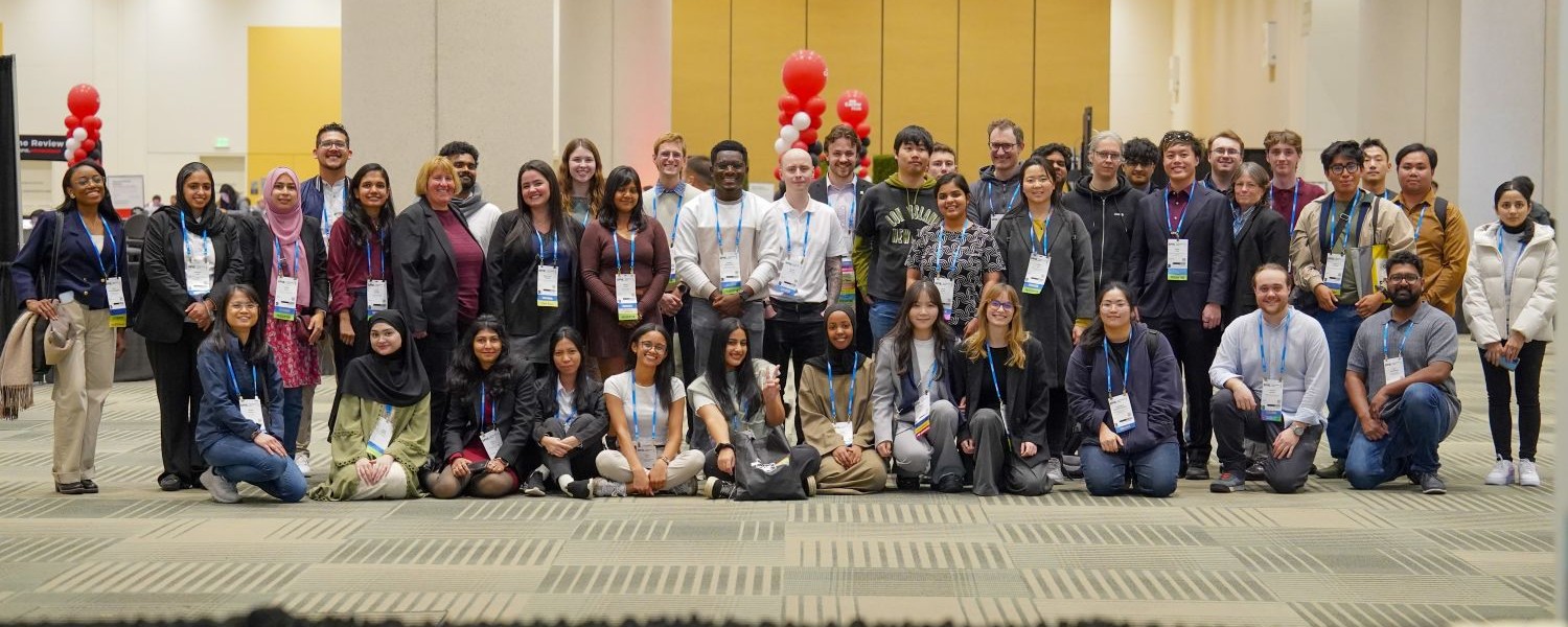 A large group of SPIE Student Scholarship and SPIE Student Conference Support Recipients posing indoors at an SPIE event, wearing conference badges.