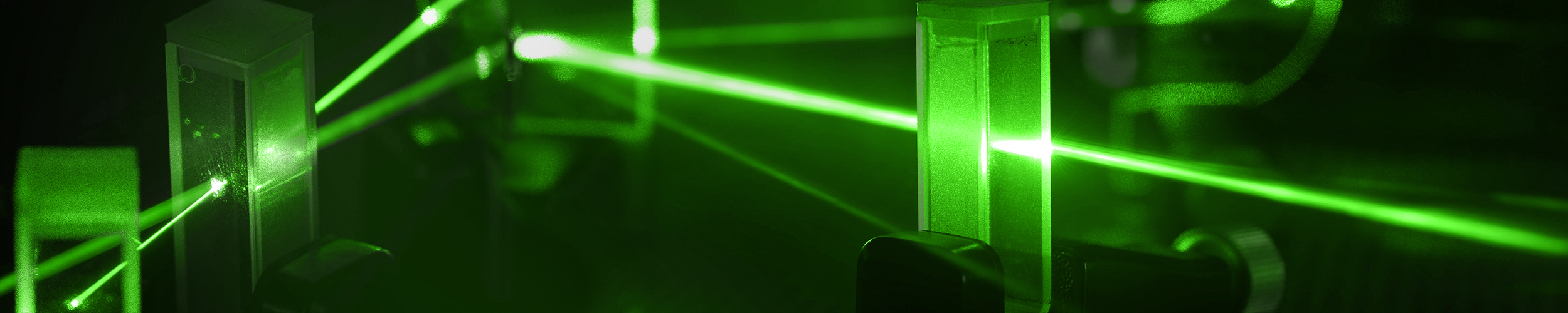 Green laser beams intersecting through mirrors and lenses in a laboratory optical setup, illustrating precision alignment and photonics experimentation.