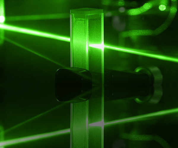 Green laser beams intersecting through mirrors and lenses in a laboratory optical setup, illustrating precision alignment and photonics experimentation.