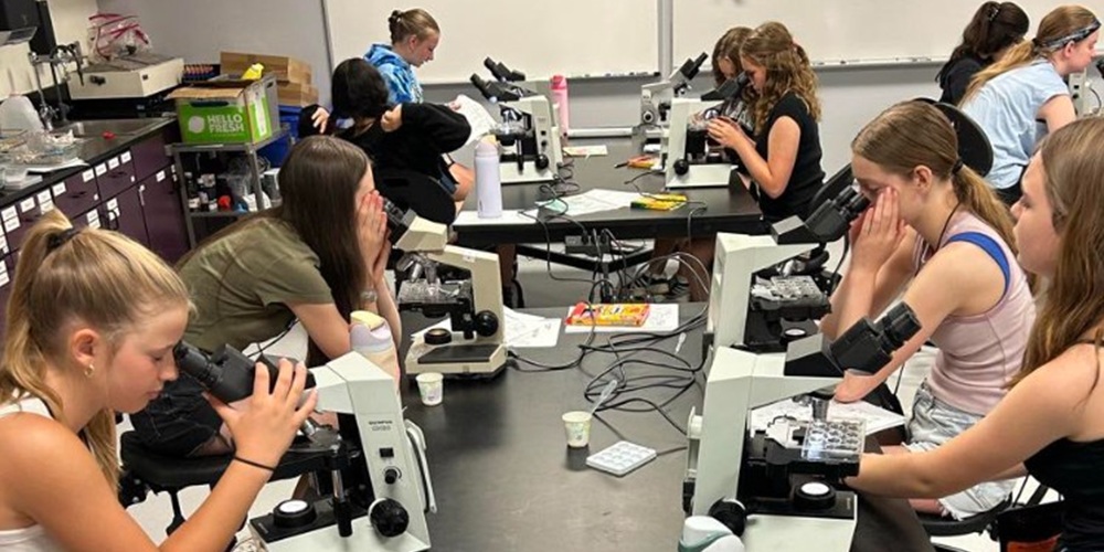 Girls ages 12- to 14-years old in a classroom look at slide through microscopes