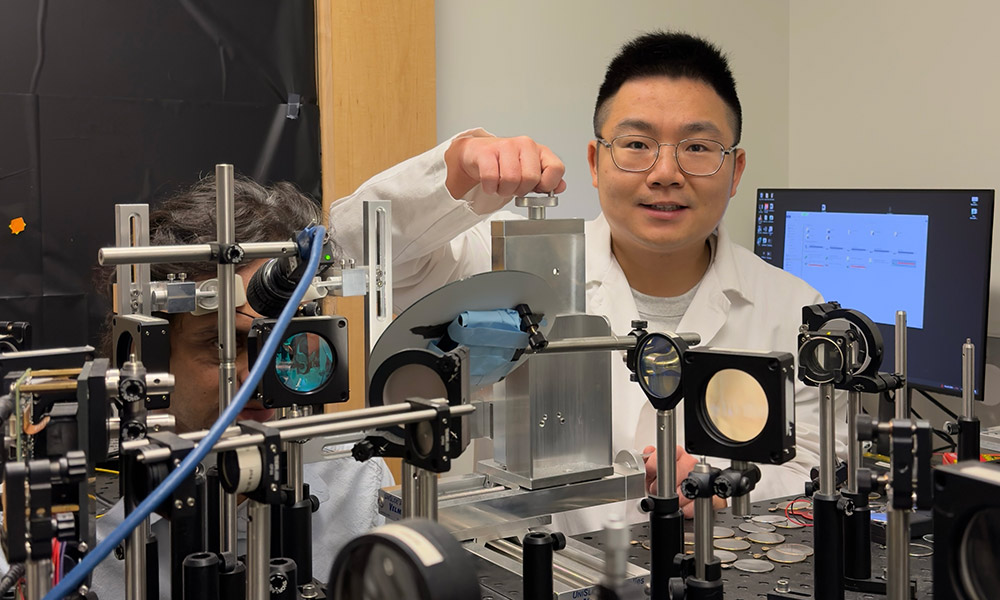 2026 SPIE-Franz Hillenkamp Postdoctoral Fellowship recipient Teng Liu, right, positions the subject, Dr. Palash Bharadwaj, at the patient-friendly optoretinography (ORG) system, and carefully aligns his pupil with the imaging beam to bring the eye into optimal focus.